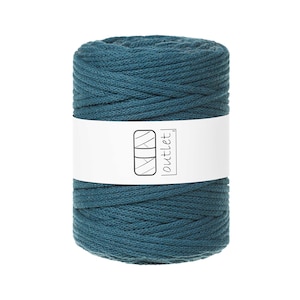 Op de afbeelding: Een cilindrische spoel van teal macramé koord. Een witte band omsluit het koord en toont een logo en het woord "outlet". Het koord lijkt strak gewikkeld, wat suggereert dat het klaar is voor knutselprojecten.