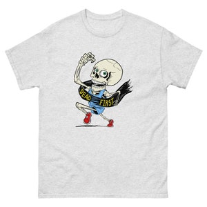 Puede incluir: Una camiseta gris con un esqueleto de dibujos animados corriendo con una pancarta que dice "Dead First".