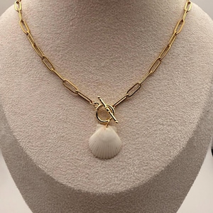 May include: Gold-toned chain necklace with a toggle clasp and a white seashell pendant. The necklace is displayed on a mannequin. The chain links are elongated and rectangular. The seashell is a natural, textured shape.