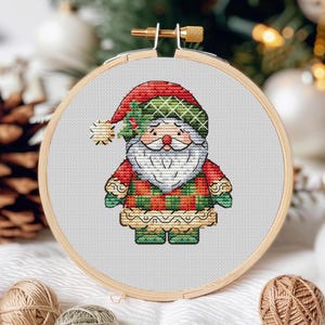 May include: A cross-stitch embroidery of Santa Claus wearing a red and green plaid shirt and a white beard. The embroidery is framed in a wooden hoop.