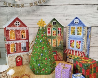 May include: A festive Christmas scene featuring handmade cross-stitch decorations. The display includes miniature houses, a Christmas tree, and wrapped gift boxes. A banner reads "MERRY CHRISTMAS".
