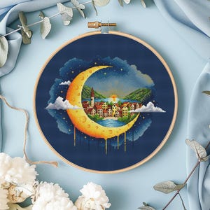 Könnte beinhalten: Ein Kreuzstichmuster eines zunehmenden Mondes mit einem tropfenden gelben Zentrum. Der Mond befindet sich über einer kleinen Stadt mit Häusern und einem Fluss. Der Hintergrund ist ein dunkelblauer Nachthimmel mit Sternen.