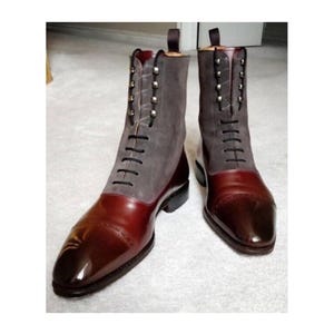 May include: A pair of two-tone leather boots. The boots have a dark burgundy toe and heel, with a gray suede upper. The boots have black laces and are accented with silver studs.