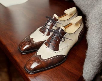 May include: A pair of brown and white leather dress shoes with wingtip detailing and lace-up fastenings.