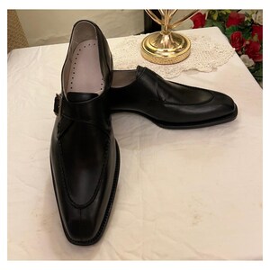 May include: A pair of black leather dress shoes with a buckle strap. The shoes have a pointed toe and a low heel.
