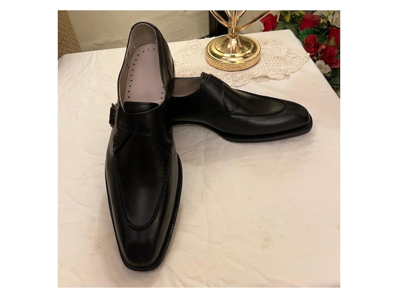 May include: A pair of black leather dress shoes with a buckle strap. The shoes have a pointed toe and a low heel.