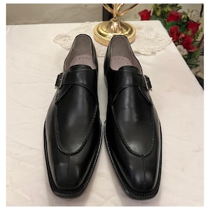 May include: A pair of black leather monk strap shoes with a buckle closure. The shoes have a pointed toe and a polished finish.