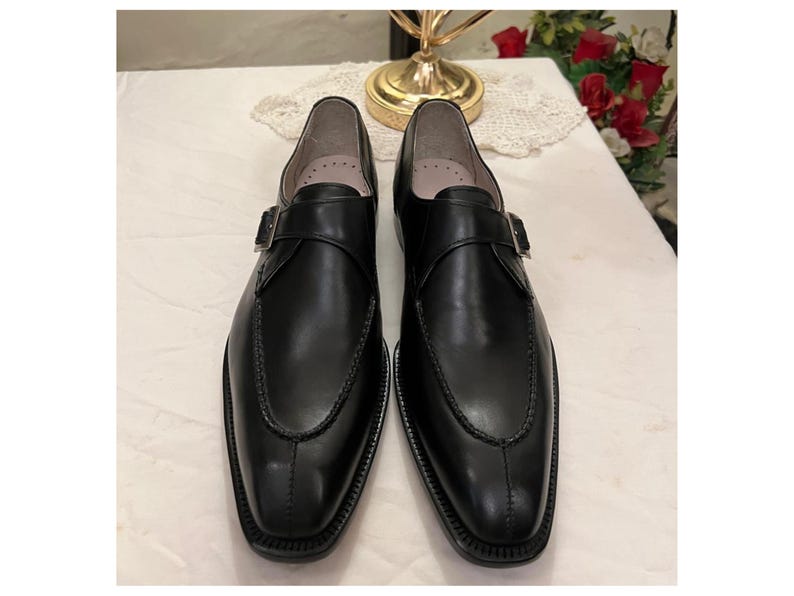 May include: A pair of black leather monk strap shoes with a buckle closure. The shoes have a pointed toe and a polished finish.