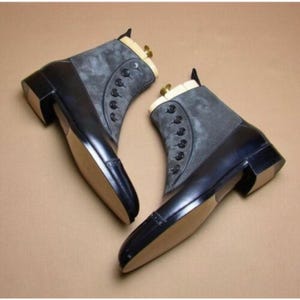 Puede incluir: Un par de elegantes botines. Los botines presentan una combinación de cuero negro y ante gris. El diseño incluye un cierre de botones en el panel de ante y un tacón cuadrado. Las suelas son de color beige claro.