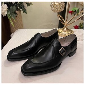May include: A pair of black leather dress shoes with a single buckle strap. The shoes have a pointed toe and a low heel.
