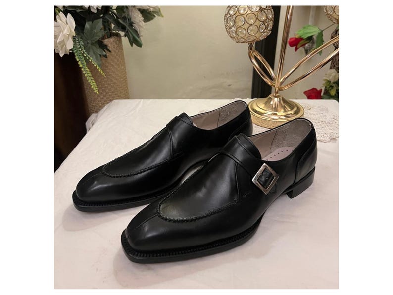May include: A pair of black leather dress shoes with a single buckle strap. The shoes have a pointed toe and a low heel.
