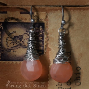 May include: A pair of silver wire wrapped earrings with pink teardrop shaped stones.
