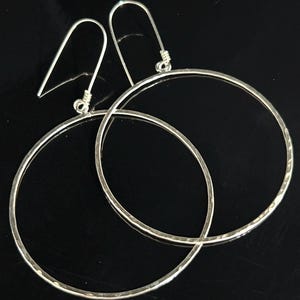 May include: A pair of silver hoop earrings with a hammered texture. The hoops are large and have a simple, elegant design.