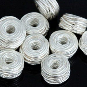 Peut inclure: Gros plan sur un groupe de perles en fil d'argent. Les perles sont rondes et ont un design en spirale. Elles sont parfaites pour la fabrication de bijoux ou d'autres projets d'artisanat.