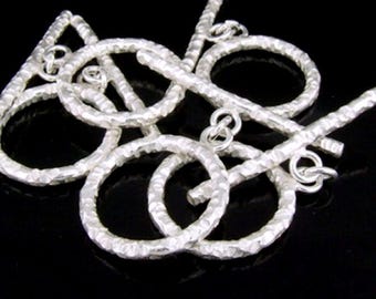 Può includere: Chiusure a scatto in argento con una texture martellata. Le chiusure sono a forma di cerchio con una barra che scorre attraverso il cerchio.