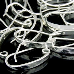 May include: A close-up of a group of silver earring hooks. The hooks are made of hammered metal and have a slightly oval shape.