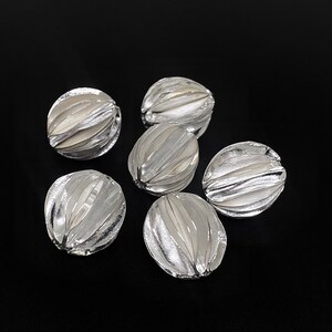 May include: Six silver-colored, oval-shaped beads with a textured, ribbed design.