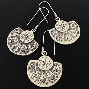 May include: A pair of silver earrings with a fan-shaped design. The earrings have a detailed floral pattern and a small circle in the center.
