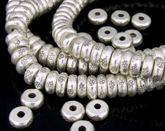 May include: A strand of silver beads with a decorative design. The beads are round and have a hole in the center. The beads are arranged in a circular pattern.
