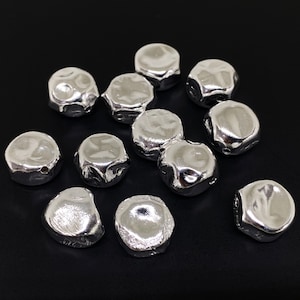 May include: A group of silver-coloured metal beads with a textured surface. The beads are round and have a slightly irregular shape.