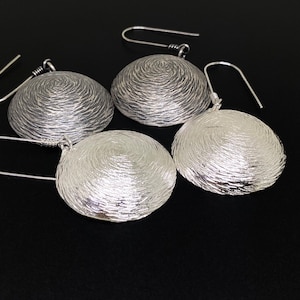 May include: A set of three silver earrings with a textured, circular design. The earrings have a simple hook closure.