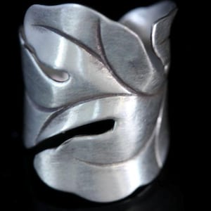 Puede incluir: Un anillo de plata con forma de hoja y superficie texturizada.