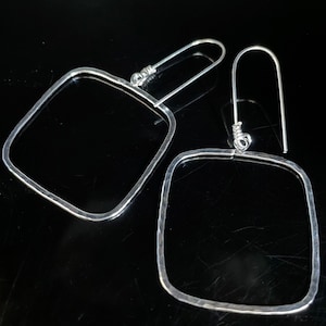 May include: A pair of silver square earrings with hammered texture. The earrings have a simple, modern design.