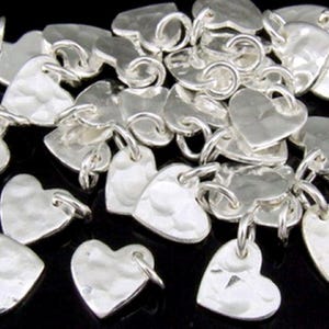 Puede incluir: Un montón de dijes de corazón plateados con textura martillada. Los dijes tienen un anillo de salto unido a la parte superior para una fácil fijación a las joyas.