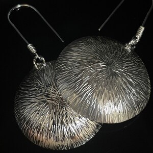 May include: A pair of silver earrings with a textured, circular design. The earrings have a simple hook closure.