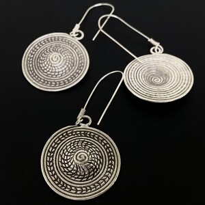 May include: A pair of silver earrings with a circular design featuring a spiral pattern. The earrings have a simple hook closure.
