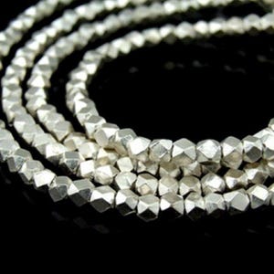 以下が含まれることがあります： ファセットカットされた幾何学的な形の銀色のビーズのストランド。ビーズはネックレスまたはブレスレットを形成するために一緒に糸でつながれています。