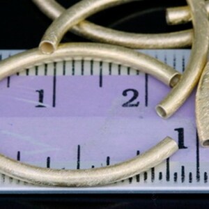 Puede incluir: Primer plano de aros de metal de color dorado, que miden aproximadamente 2,5 cm de di&aacute;metro, con una superficie ligeramente texturizada. Los aros est&aacute;n dispuestos sobre una regla con marcas en cent&iacute;metros.