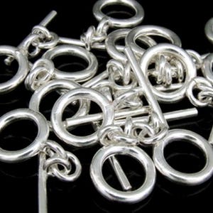 Może przedstawiać: Srebrne klamry zamykane z okrągłym pierścieniem i prostym prętem. Klamry są połączone ze sobą w stos.
