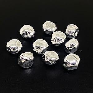 May include: Ten silver-coloured metal beads with a slightly irregular, rounded shape. The beads have a smooth, shiny finish.
