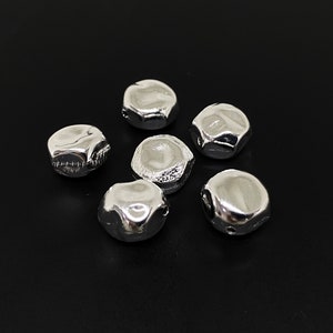 May include: Six silver-coloured metal beads with a textured surface. The beads are round and have a slightly irregular shape.