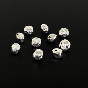 May include: Ten silver-toned metal beads with a hole in the centre. The beads are irregularly shaped and have a slightly textured surface.