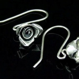 May include: A pair of silver rose earrings with a hook closure. The roses are detailed and have a three-dimensional look.