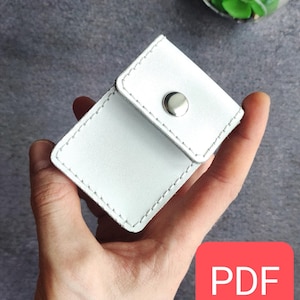 Op de afbeelding: Een klein wit leren portemonnee met een klep sluiting en een zilveren knoop. De portemonnee wordt in een hand gehouden. De afbeelding heeft het woord "PDF" in een rood vak.