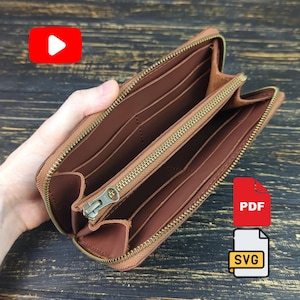 May include: A brown leather wallet with a wrap-around brass zipper, featuring multiple interior card slots, a central zippered coin compartment, and open bill pockets. The wallet is open to reveal the smooth, tan-colored leather interior lining.