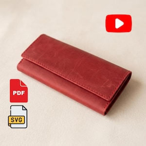 May include: A rectangular red leather wallet with a fold-over flap closure and visible stitching along the edges. The surface of the wallet has a matte, slightly distressed texture. The image includes a red YouTube icon, a red PDF icon, and a white SVG icon.