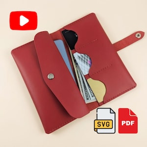 May include: A red leather wallet featuring a snap button closure, multiple interior card slots, and a dedicated compartment for paper currency. The wallet is shown open, revealing its internal structure and storage capacity for cards and cash.