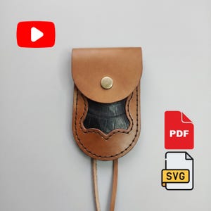 May include: A tan leather pouch with a rounded flap and a brass-colored snap button closure. The center features a black textured inlay with a scalloped edge. A thin leather strap extends from the bottom. Includes YouTube, PDF, and SVG icons.