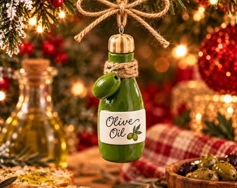 Può includere: Un ornamento in ceramica a forma di bottiglia di olio d'oliva verde appeso a un fiocco di corda di juta. La bottiglia presenta un'etichetta bianca con la scritta nera Olive Oil e una piccola illustrazione di un'oliva verde.