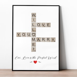 Puede incluir: Una impresión enmarcada en blanco con las palabras "Will You Marry Me?" deletreadas con fichas de Scrabble. Las fichas están dispuestas en formato de crucigrama. El texto "Our Love is the Perfect Word" está escrito debajo del crucigrama.