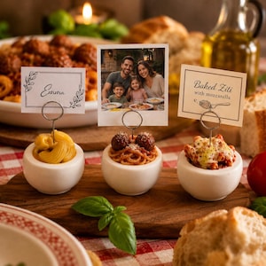 May include: Three white ceramic bowls holding food samples, each featuring a wire stand with a card. The cards display the text Emma, a family photo, and Baked Ziti with mozzarella. The bowls contain macaroni, spaghetti with meatballs, and pasta.