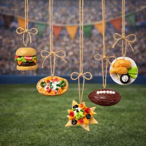 May include: A collection of food-themed ornaments hanging from twine, including a hamburger, pizza, nachos, a football, and fried chicken. The ornaments are set against a blurred background of a football stadium and colorful pennants.