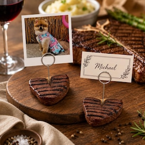 Peut inclure: Deux morceaux de steak grillés en forme de cœur servant de porte-noms. L'un tient une photo carrée d'un petit chien poilu en robe bleue, et l'autre tient une carte blanche rectangulaire avec le nom Michael imprimé en écriture noire.