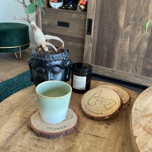Könnte beinhalten: Drei Holz-Untersetzer mit den Namen Monza, Zandvoort und einem dritten unleserlichen Namen. Die Untersetzer befinden sich auf einem Holztisch mit einer grünen Keramiktasse und einer braunen Glaskerze.