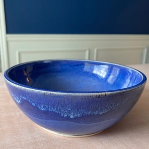 May include: A large, blue ceramic bowl with a white glaze. The bowl has a slightly uneven rim and a subtle, mottled texture.