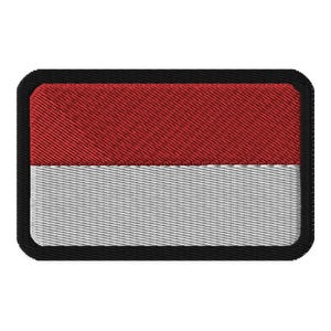 Op de afbeelding: Een rood en wit geborduurde patch met een zwarte rand. De patch is rechthoekig en heeft een geweven textuur.